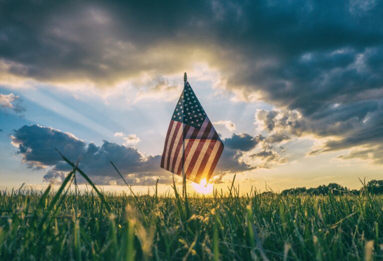 american flag set in grass with sunrise in the background