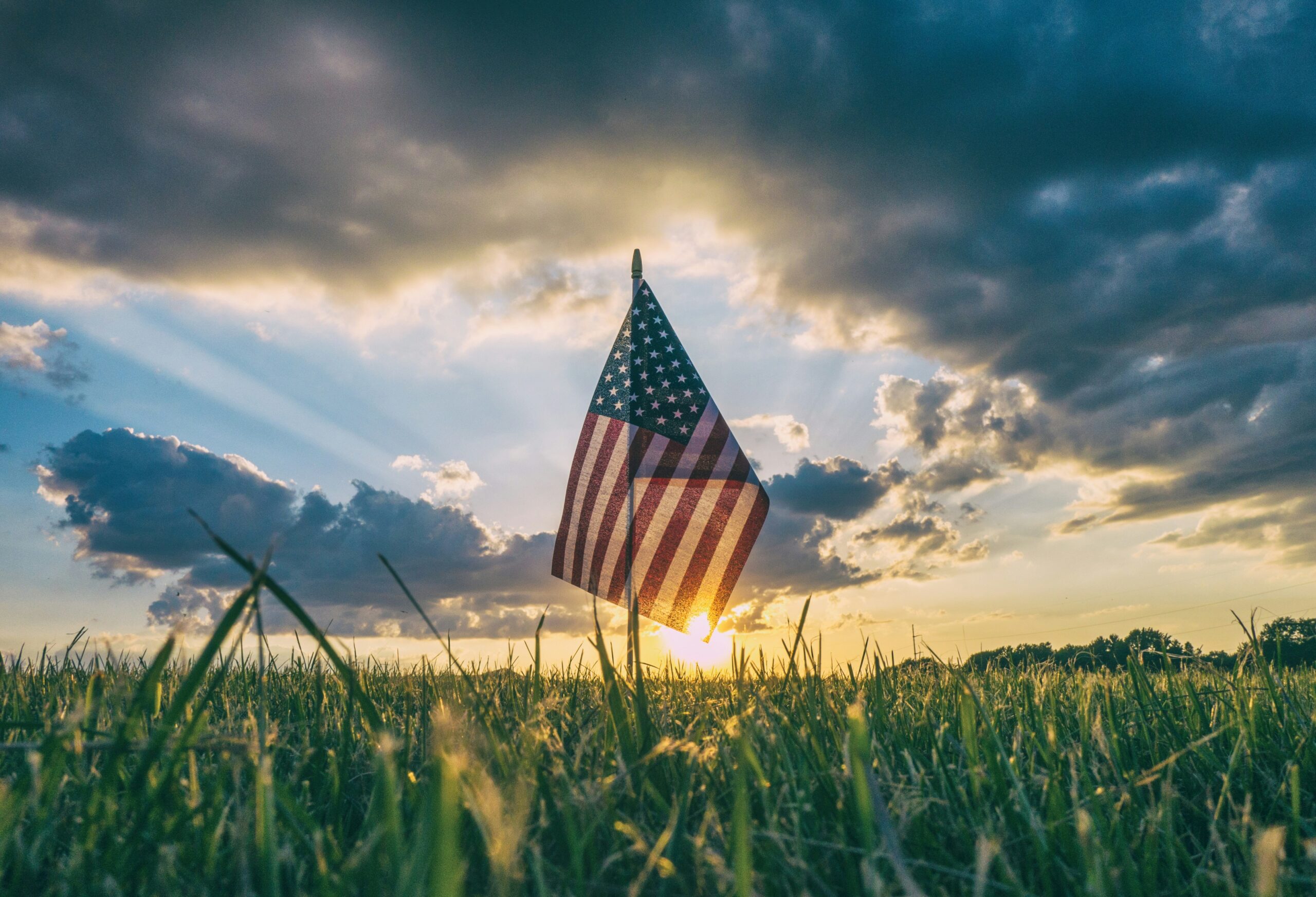 american flag set in grass with sunrise in the background
