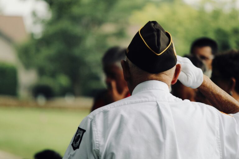 older vet with uniform on and hat saluting with right hand which is gloved