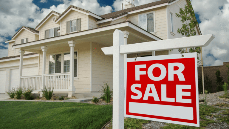 a for sale sign in the foreground with a white house with a manicured lawn in the background